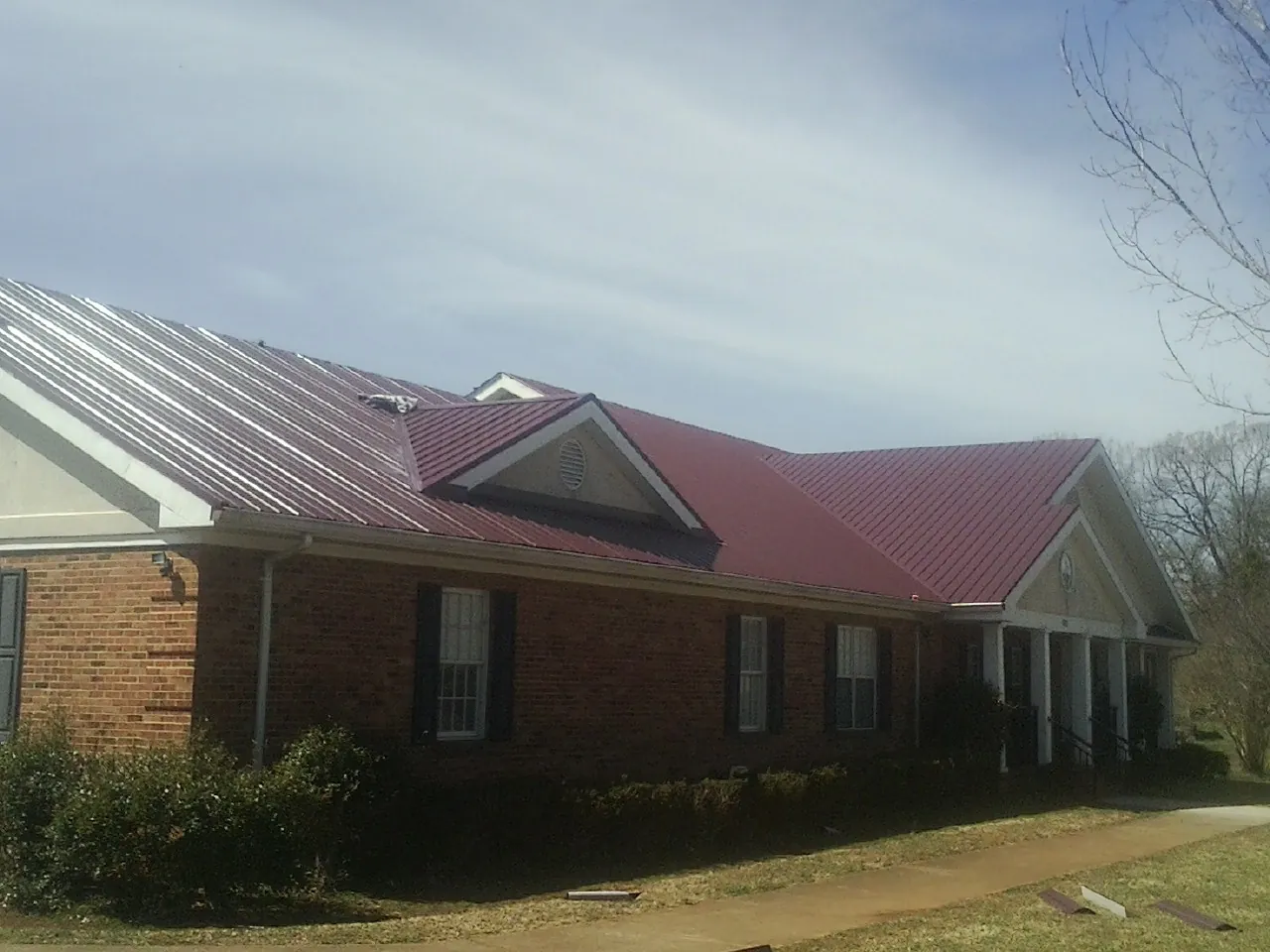 Red metal roof with gabled entries on a long brick building, from a Hail Damage Roof Repair job in Ramah