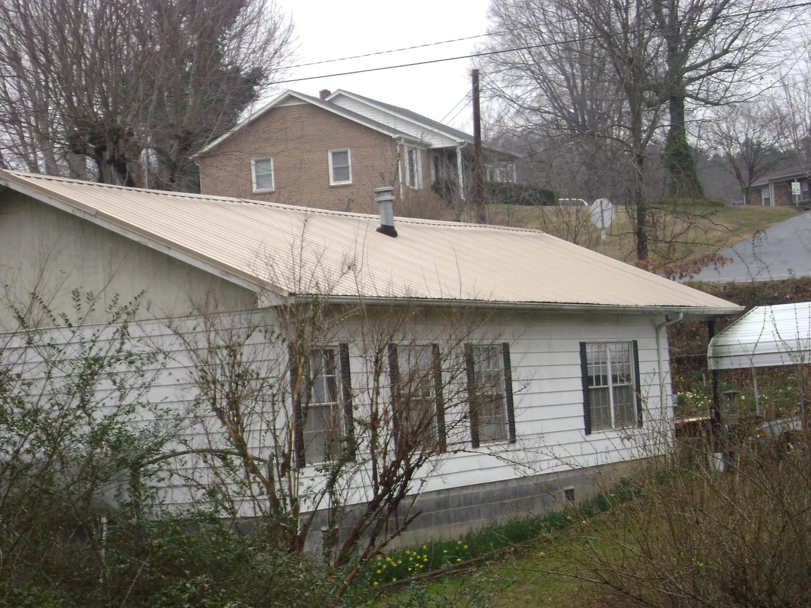 Tan metal roof on a white sided house set into a hillside — Commercial Roofing by Roofing Brothers in Ramah
